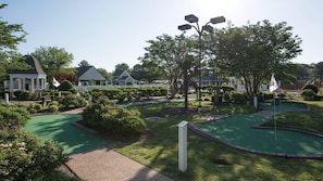 A miniature golf course with a gazebo, neatly trimmed bushes, and a white fence.