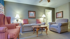 A living room with a sofa, armchairs, a coffee table, lamps, and framed pictures on the wall.