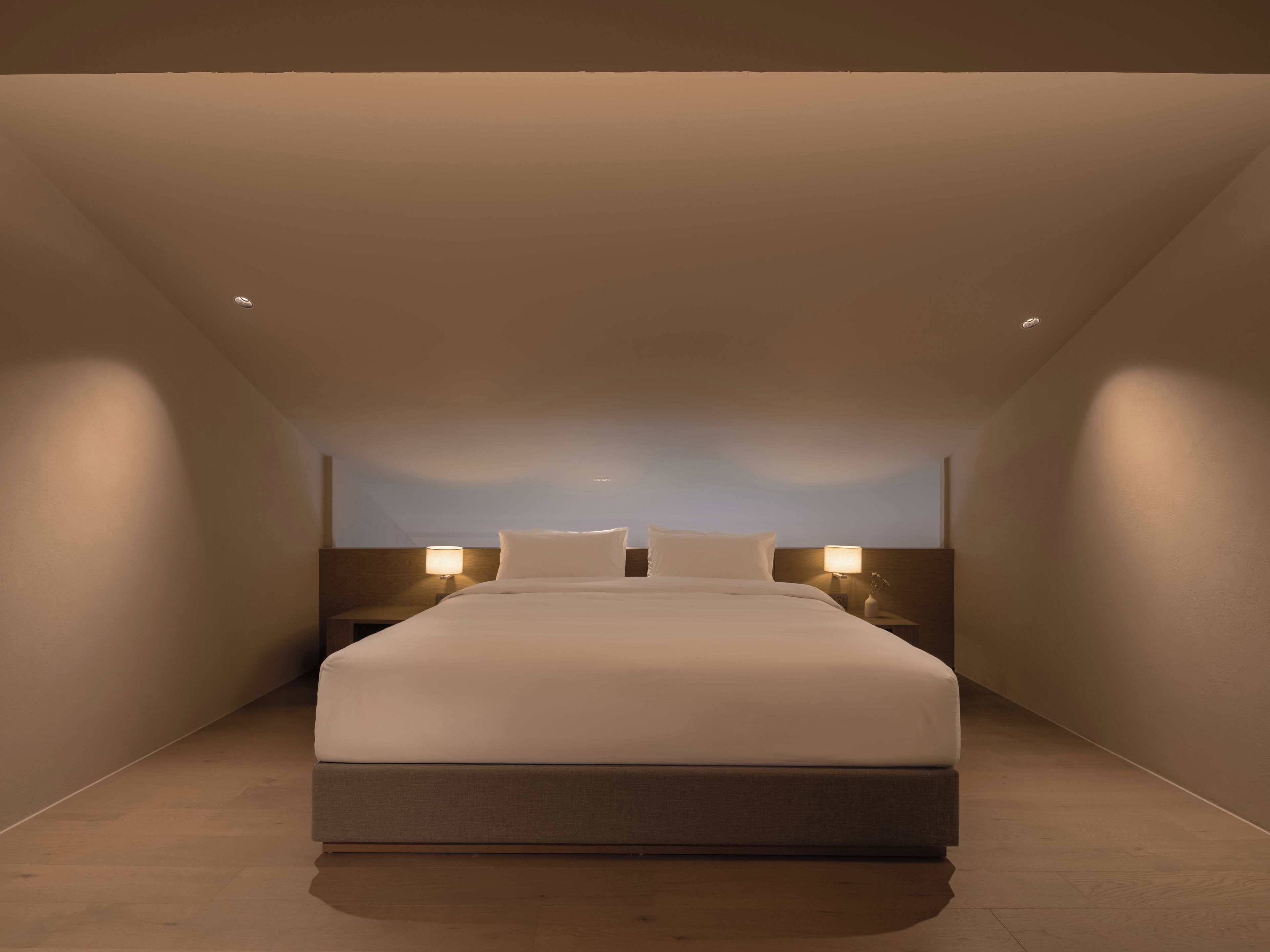 Una habitación de hotel moderna con una cama grande, dos lámparas de noche y un techo inclinado.