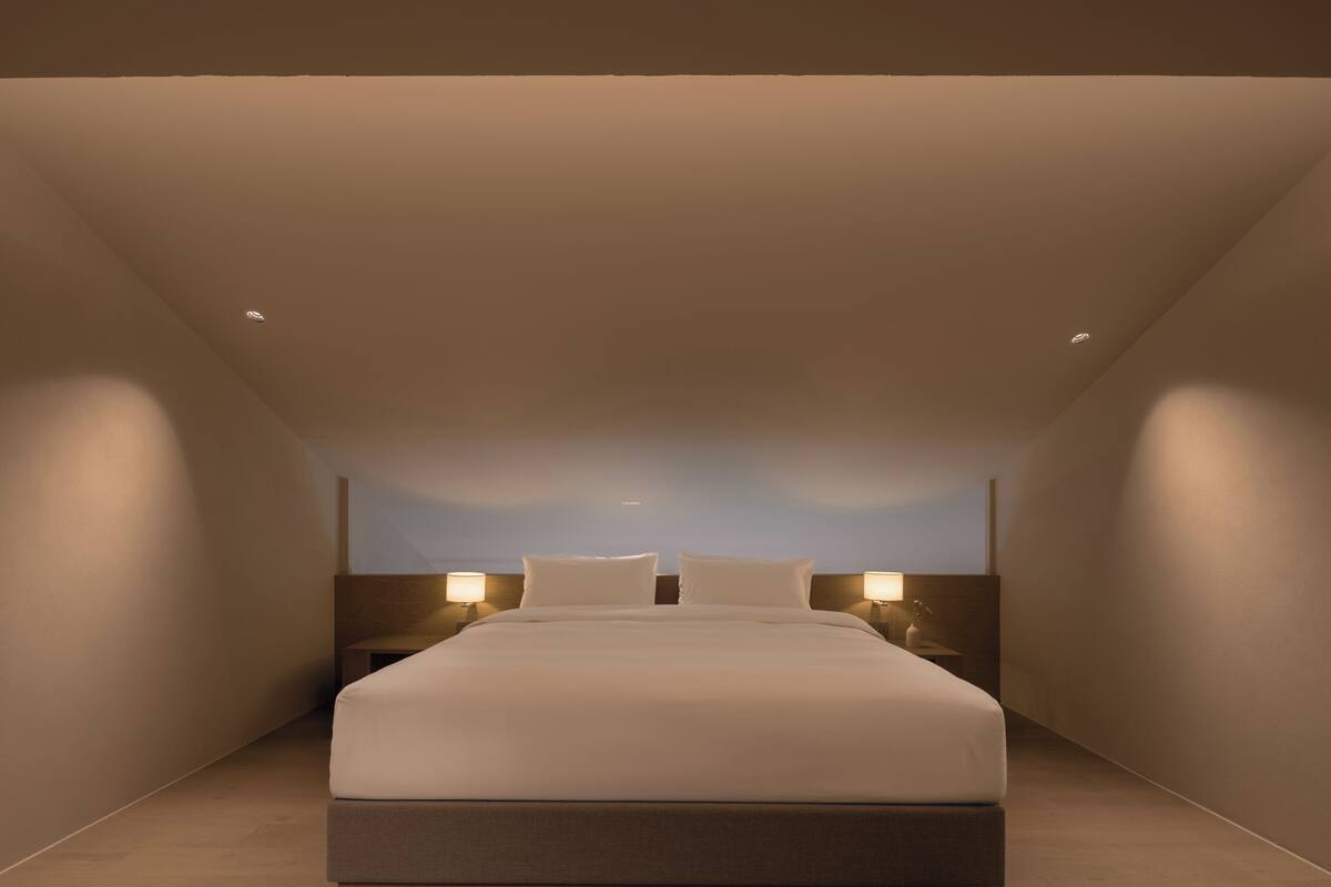 Et moderne hotelværelse med en stor seng, to sengeborde med lamper og et skråt loft.