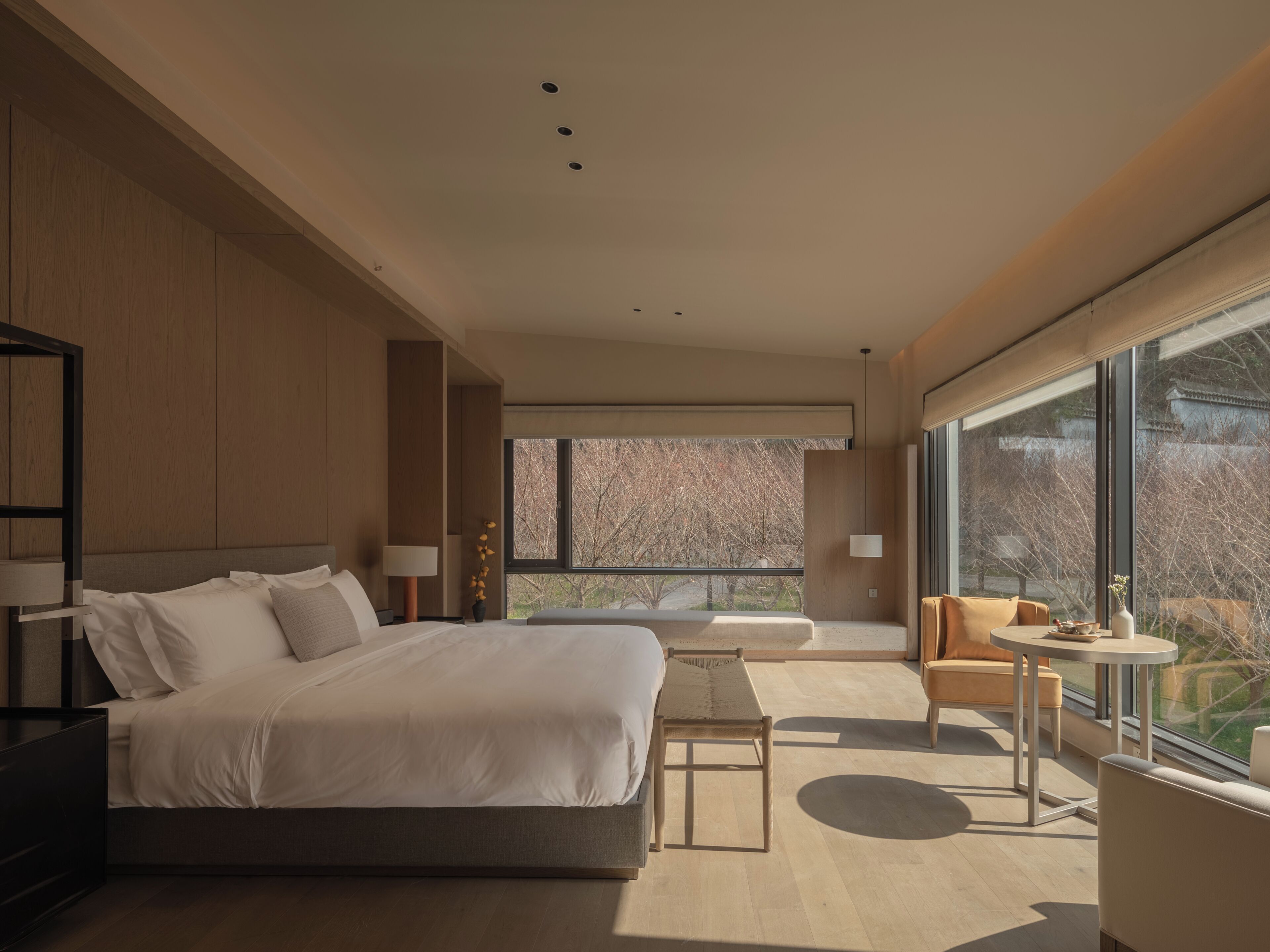 Un hotel moderno con una cama grande, una mesita pequeña, un sofá y vistas al exterior a través de amplios ventanales.