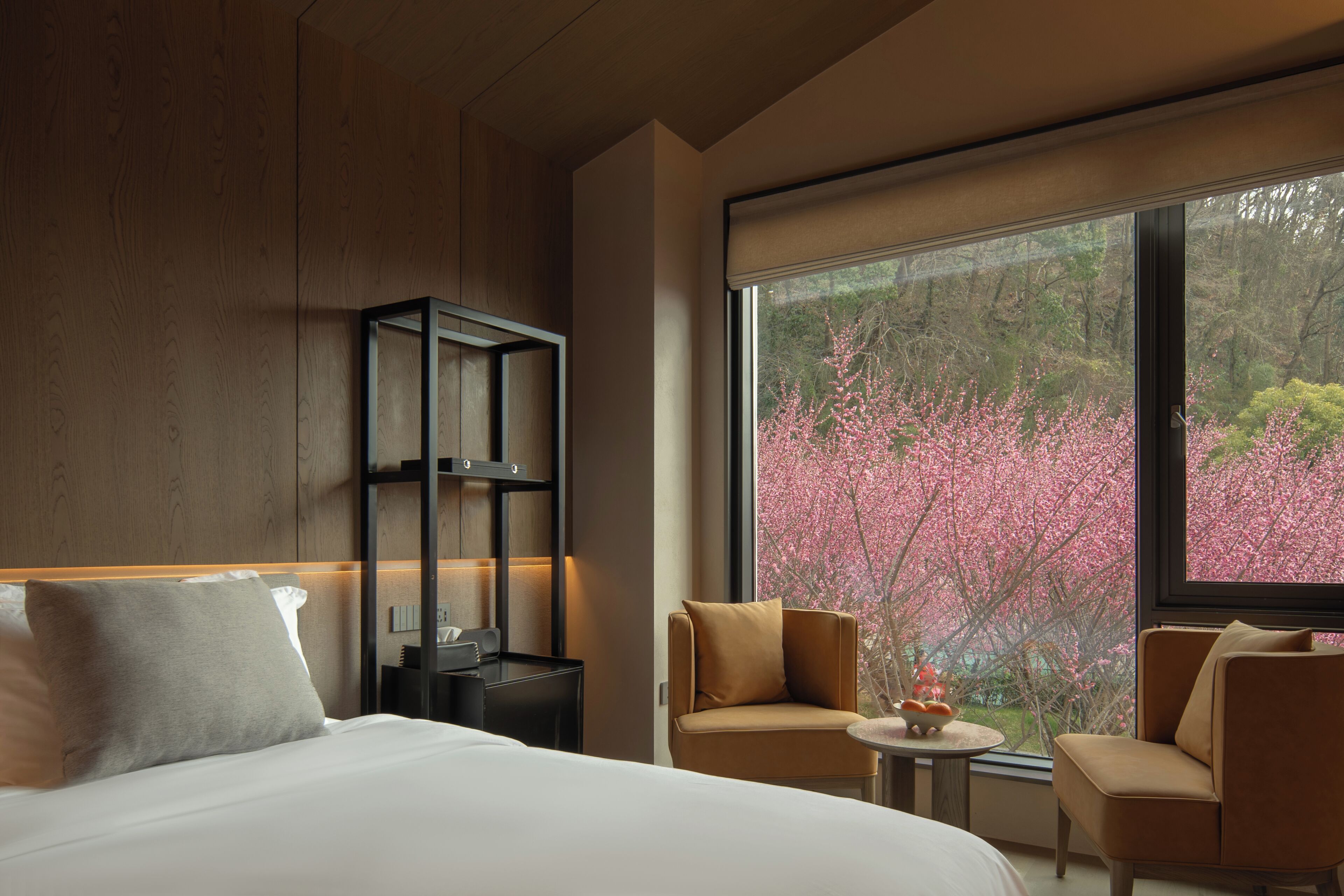 Una habitación de hotel moderna con un ventanal grande, una cama, una zona de estar y una pequeña mesa.
