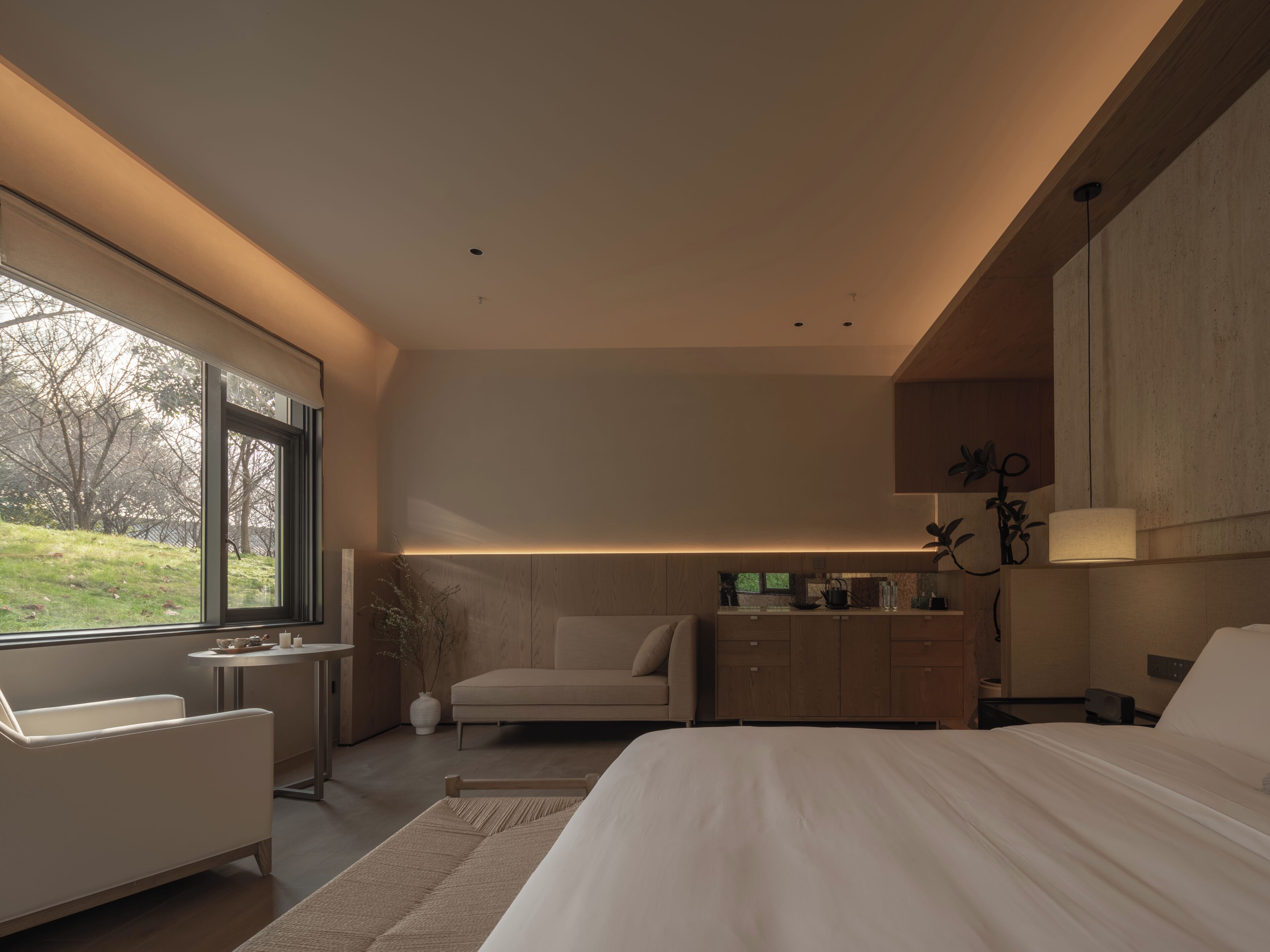 Un dormitorio moderno con una cama grande, zona de estar, escritorio y vistas al exterior.
