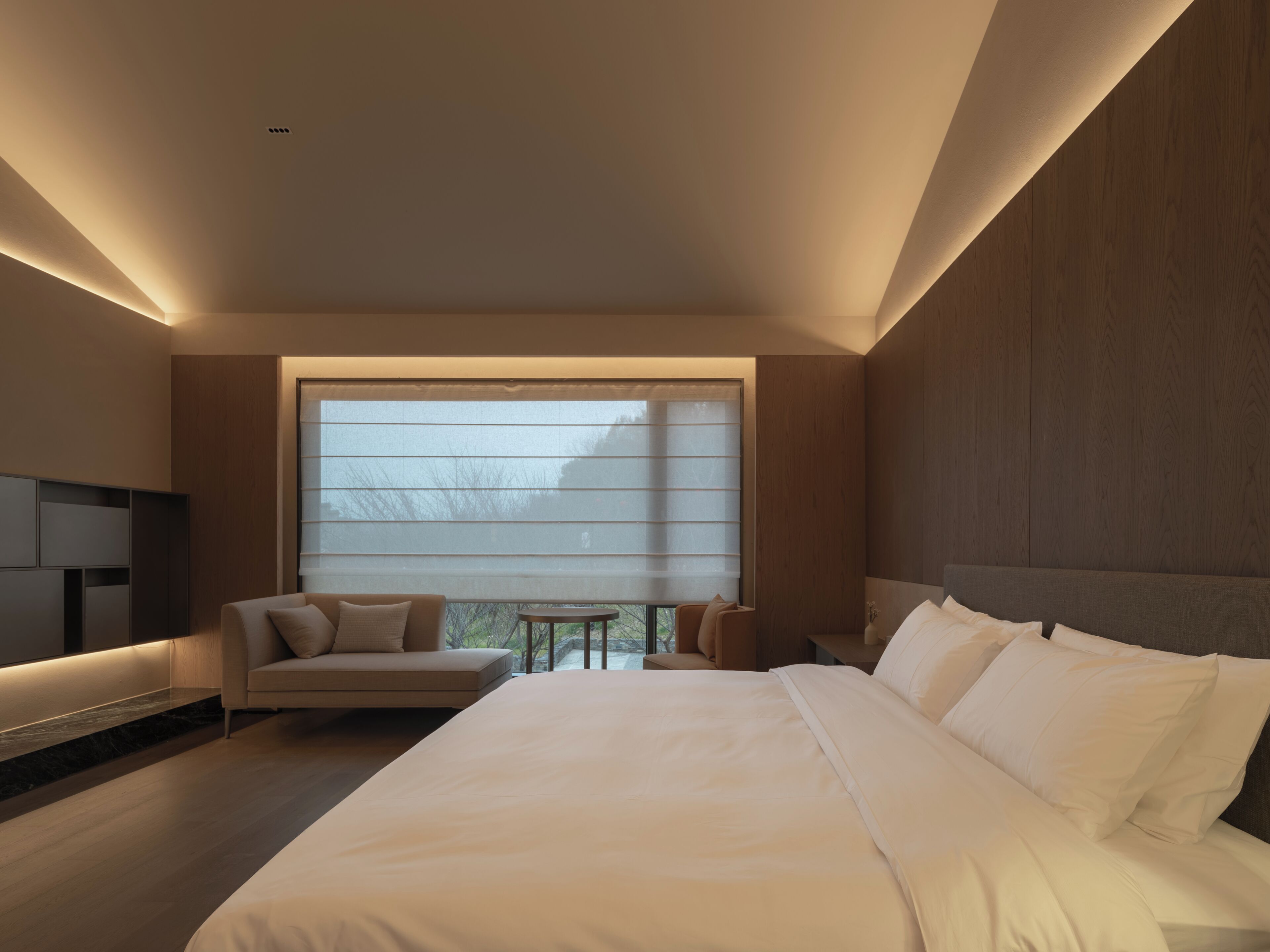 Un dormitorio moderno con una cama grande, un sofá, una mesita y un televisor.