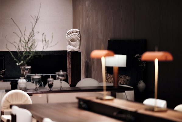 Ein moderner Essbereich mit einem Holztisch, Stühlen, einer Skulptur und zwei Lampen.