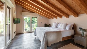 A bedroom with a wooden ceiling, a bed with white bedding, a nightstand, and a TV mounted on the wall. - Riflesso del Lago - by MyHomeInComo (Menaggio)