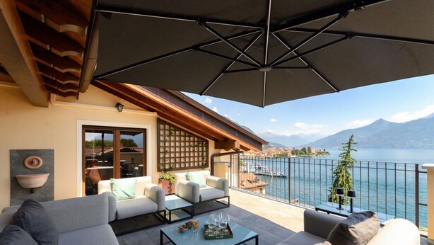A terrace with a sofa, coffee table, and umbrella, overlooking a lake and mountains. - Riflesso del Lago - by MyHomeInComo (Menaggio)