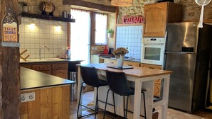 A rustic kitchen with wooden cabinets, a stainless steel refrigerator, and a hanging light fixture. - Country house in Périgord with swimming pool (Beaumontois en Périgord)