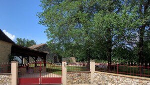 A gated entrance with a red gate, a stone wall, and a covered area with a tiled roof. - Country house in Périgord with swimming pool (Beaumontois en Périgord)