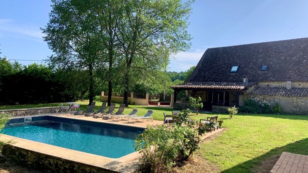 A swimming pool with lounge chairs, a stone wall, and a house with a tiled roof. - Country house in Périgord with swimming pool (Beaumontois en Périgord)