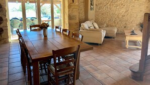 A rustic interior with a wooden dining table, chairs, a sofa, and a stone wall. - Country house in Périgord with swimming pool (Beaumontois en Périgord)