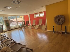 Une pièce avec un plancher en bois, un mur rouge et une grande fenêtre. Plusieurs chaises sont disposées pour permettre aux gens de s’asseoir.