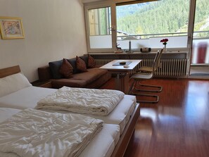 Une chambre d’hôtel comprenant un lit, un canapé, une petite table avec une chaise, un radiateur et une fenêtre donnant sur une forêt.