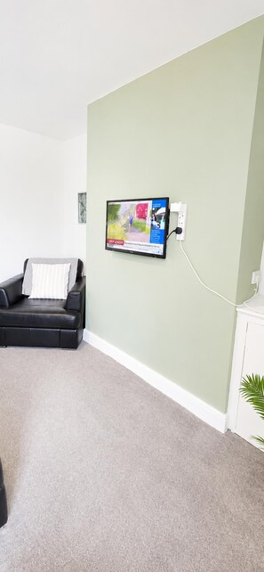 A living room with a black leather sofa, a flat-screen TV mounted on the wall, a white cabinet, and a green accent wall. - House Sleeps 7 With Wifi (Gateshead)