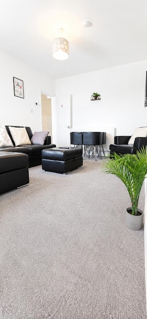 A modern living room with a sofa, ottoman, and chairs, a potted plant, and a ceiling light fixture. - House Sleeps 7 With Wifi (Gateshead)