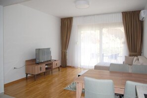 A modern living room with a wooden TV stand, a dining table with chairs, and a sofa set. - Status M Apartments 89 (Becici)