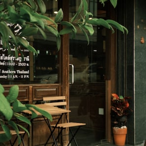 A wooden bench outside a building with a glass door, a potted plant, and a sign with text. - Large Room Near Grand Palace (Bangkok)
