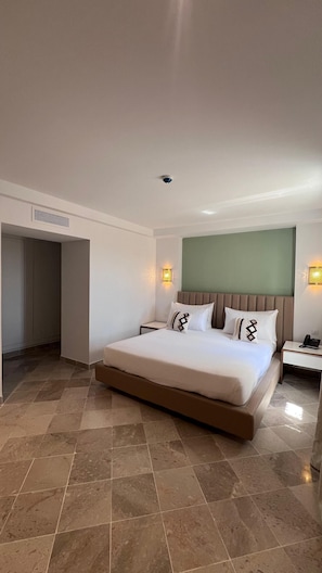 A modern hotel room with a large bed, a desk, and a green accent wall.