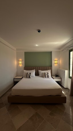 A large bed with a headboard, two bedside tables, and wall-mounted lights.. Tej El Medina