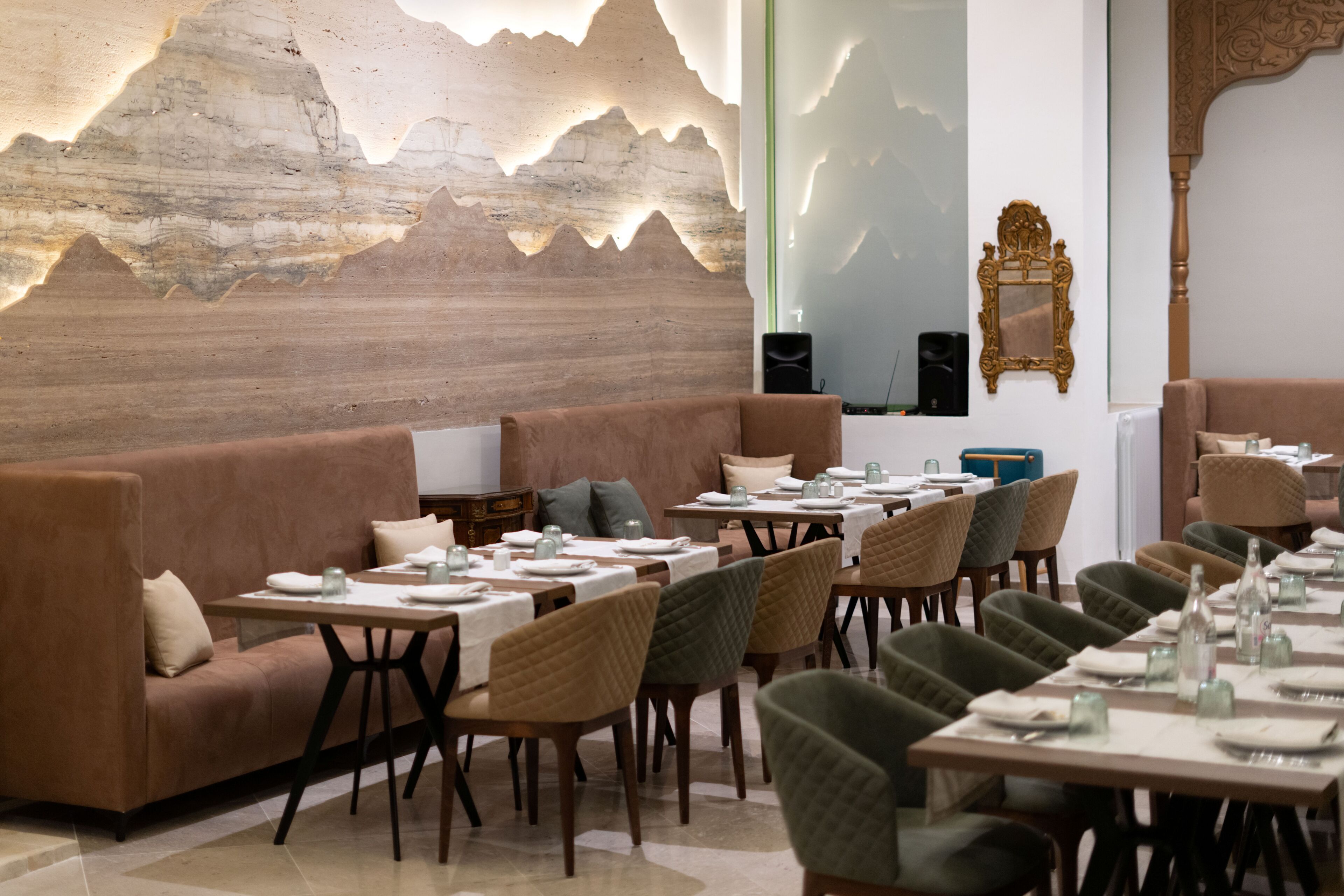 A restaurant with a long dining table, cushioned seating, and a decorative wall.