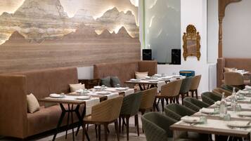A restaurant with a long dining table, cushioned seating, and a decorative wall.