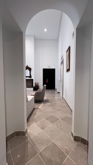 A hallway with a tiled floor, a sofa, a chair, and a door at the end. - Tej El Medina (Le Kef)