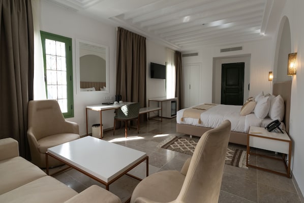 A hotel room with a bed, a desk, a chair, a sofa, and a television.