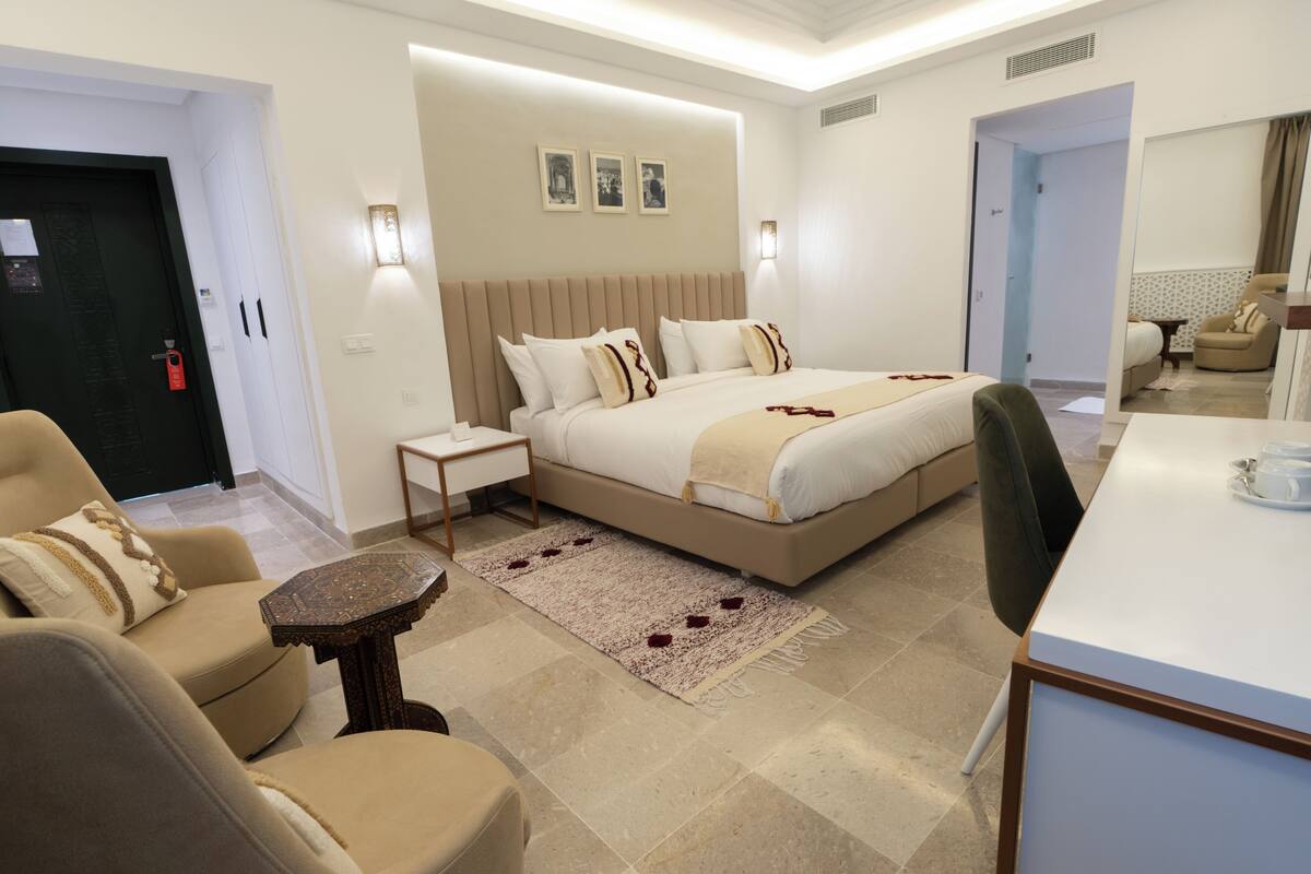 Una habitación de hotel con una cama, dos sillas, una mesita, una mesita de noche y un espejo.