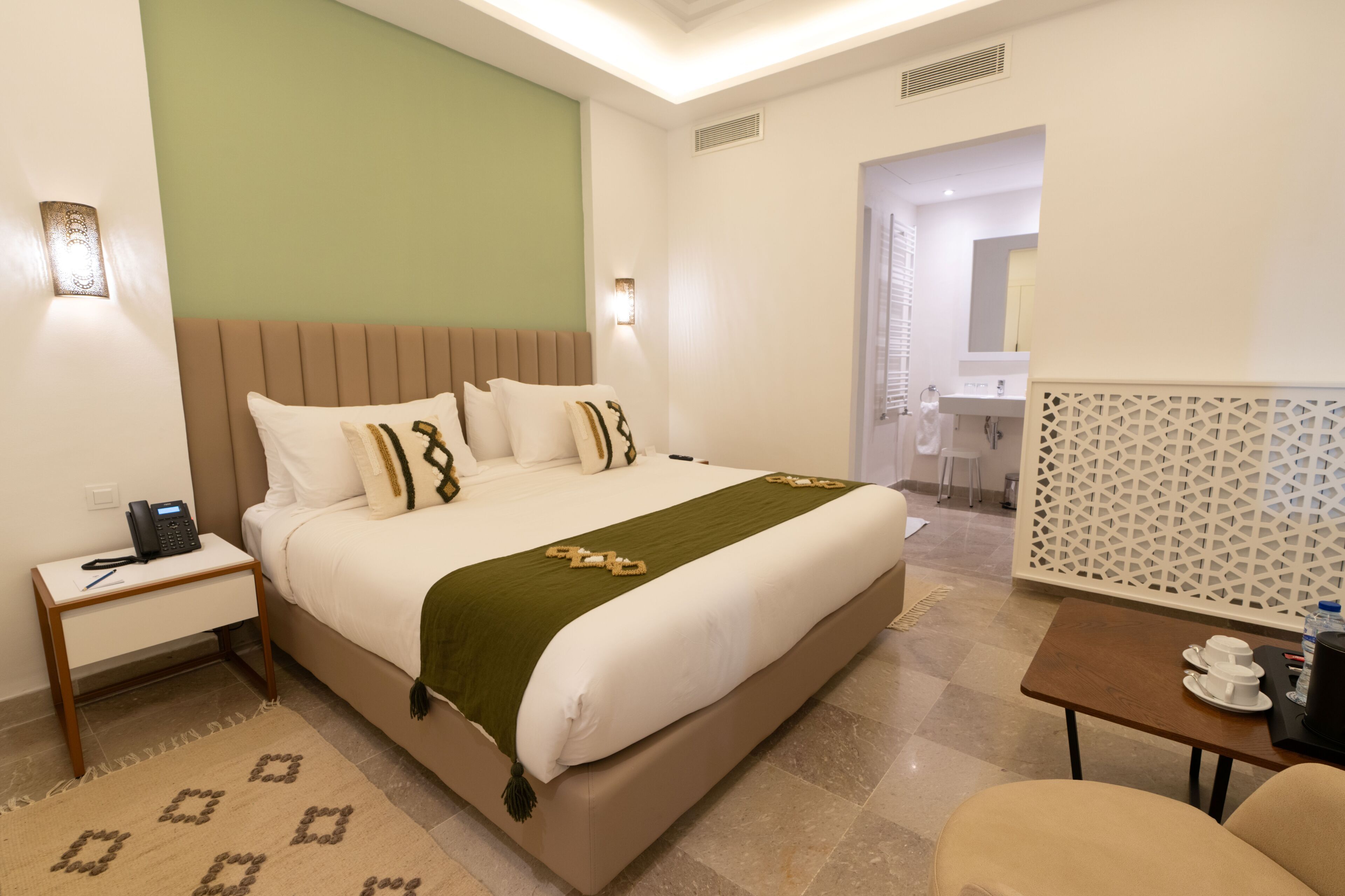Una habitación de hotel con cama, mesita de noche, lámpara y una pequeña mesa con tazas.