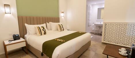 Una habitación de hotel con cama, mesita de noche, lámpara y una pequeña mesa con tazas.