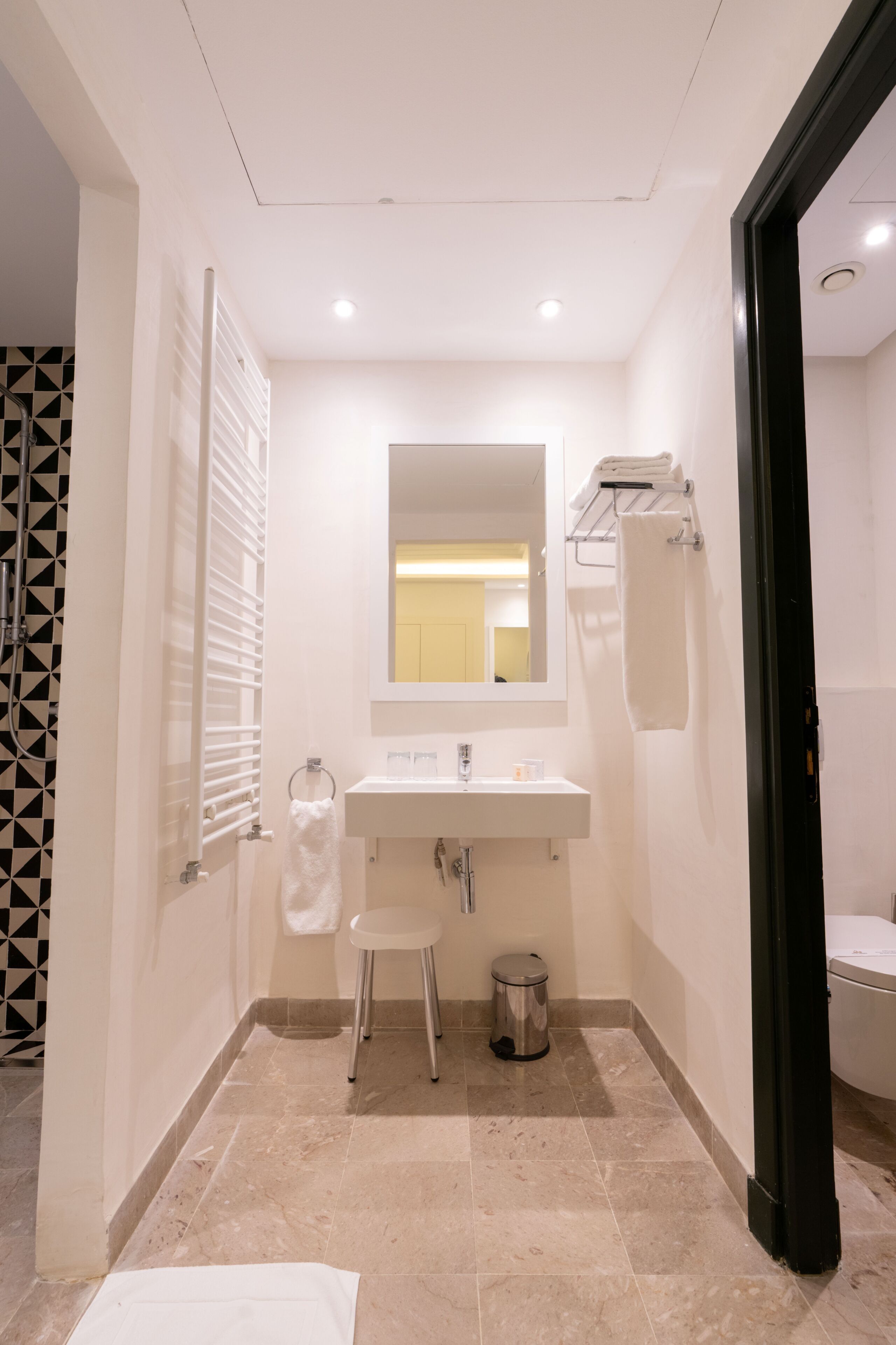 Een badkamer met een wit wastafelmeubel, spiegel, handdoekhouder en een klein krukje.