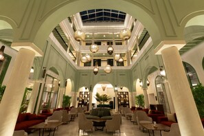 A spacious lobby with multiple seating areas, a central staircase, and a high ceiling with hanging lamps.