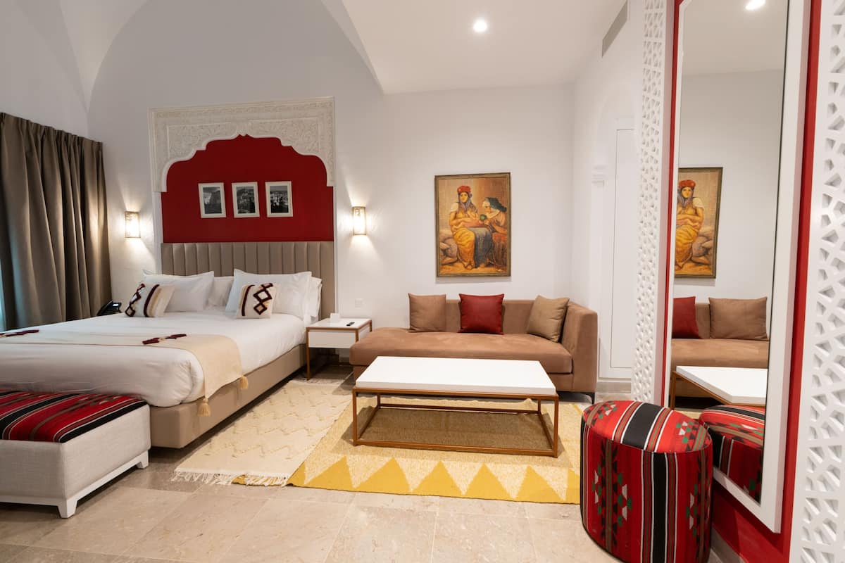 Habitación de hotel con cama, sofá, mesa de centro, mesita de noche y un cuadro colgado en la pared.