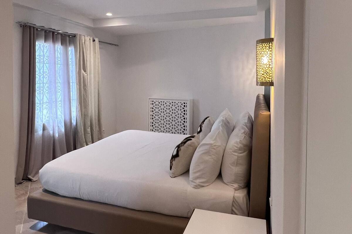 Una habitación de hotel moderna con una cama grande, una mesita de noche y una lámpara de pared decorativa.