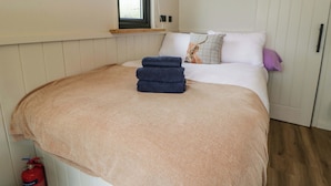 A bedroom with a bed, a window, a fire extinguisher, and a wooden ceiling. - The Hut (Llandysul)