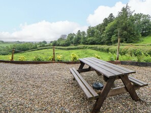 Ein Picknicktisch mit Bänken, umgeben von Kies, mit Blick auf grüne Hügel und Bäume.