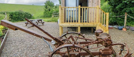 A rustic wooden structure with a balcony, a wooden bench, and a large, rusty mechanical wheel.