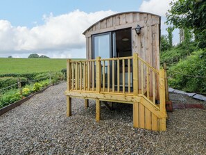 Eine Holz-Blockhütte mit Balkon, Kiesgrund und einem grünen Feld im Hintergrund.