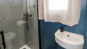 A bathroom with a shower, a sink, and a window with a curtain. - The Hut (Llandysul)