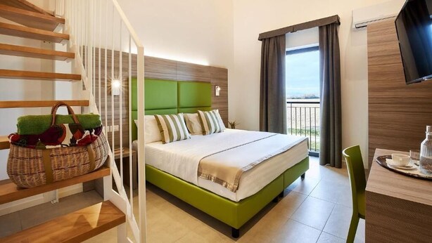 A hotel room with a bed, a TV, a balcony, and a staircase. - Brussa Horse Oasi (Caorle)
