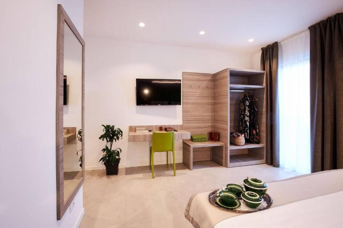 Una habitación de hotel moderna con una cama, un escritorio, un televisor, un armario y una planta pequeña.