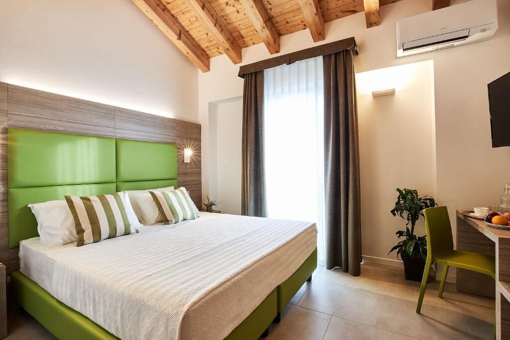 Une chambre avec une tête de lit verte, un lit avec des oreillers à rayures, un bureau avec une chaise et une plante en pot.