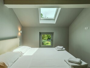 A bedroom with a skylight, a bed with white linens, a small window, and a wall-mounted light. - Apartment Zani by Interhome (Lago di Mezzola)