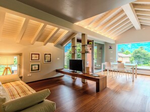 A modern living room with a wooden floor, a sofa, a TV, and a dining area with a table and chairs. - Apartment Zani by Interhome (Lago di Mezzola)