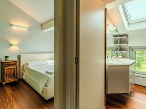 Un dormitorio con cama, mesita de noche y ventana con vista a follaje.