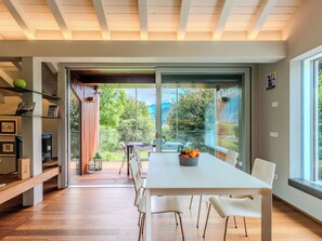 Un comedor moderno con una mesa grande, sillas blancas y vistas a un jardín a través de amplios ventanales.