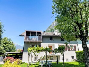 Ein zweistöckiges Haus mit Balkon, einem Garten und einem Berg im Hintergrund.