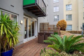 Een woongebouw met een houten terras, plantenpotten en een omheind gebied.
