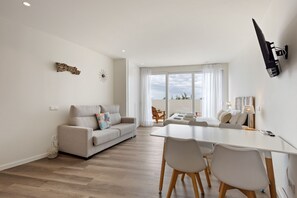 Ein modernes Wohnzimmer mit Sofa, Esstisch und Stühlen. Ein Balkon bietet einen Ausblick.