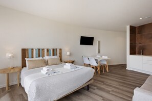 Ein modernes Hotelzimmer mit Bett, Schreibtisch, Stühlen, Fernseher und Küchenzeile.